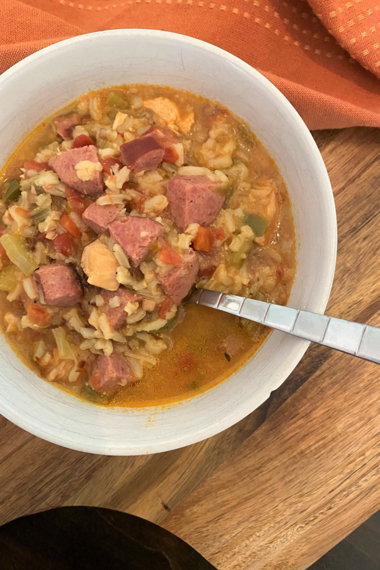 Gumbo in a white bowl with a spoon on a wooden cutting board