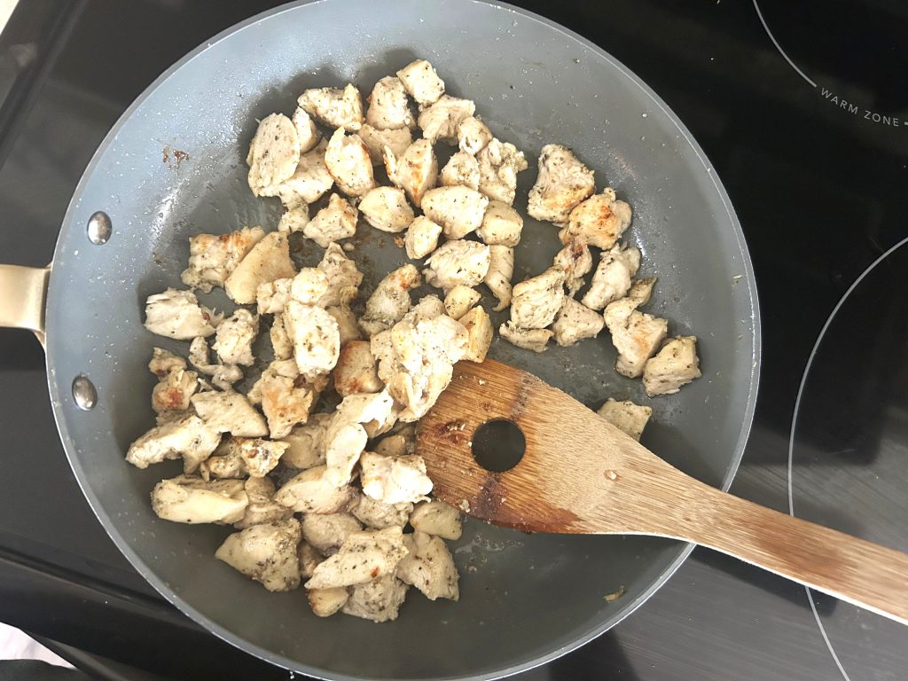 A stove top with a skillet pan and a wooden spoon, cooking chopped chicken