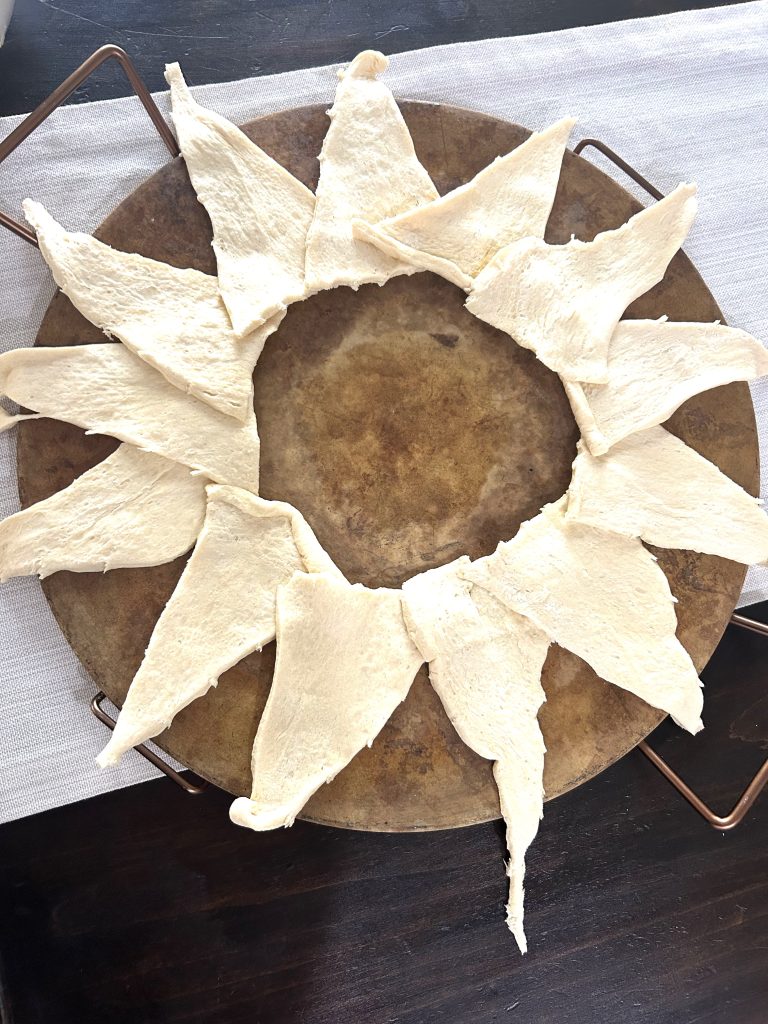 A round baking stone on a gray table runner shaped like a sun to make chicken broccoli braid