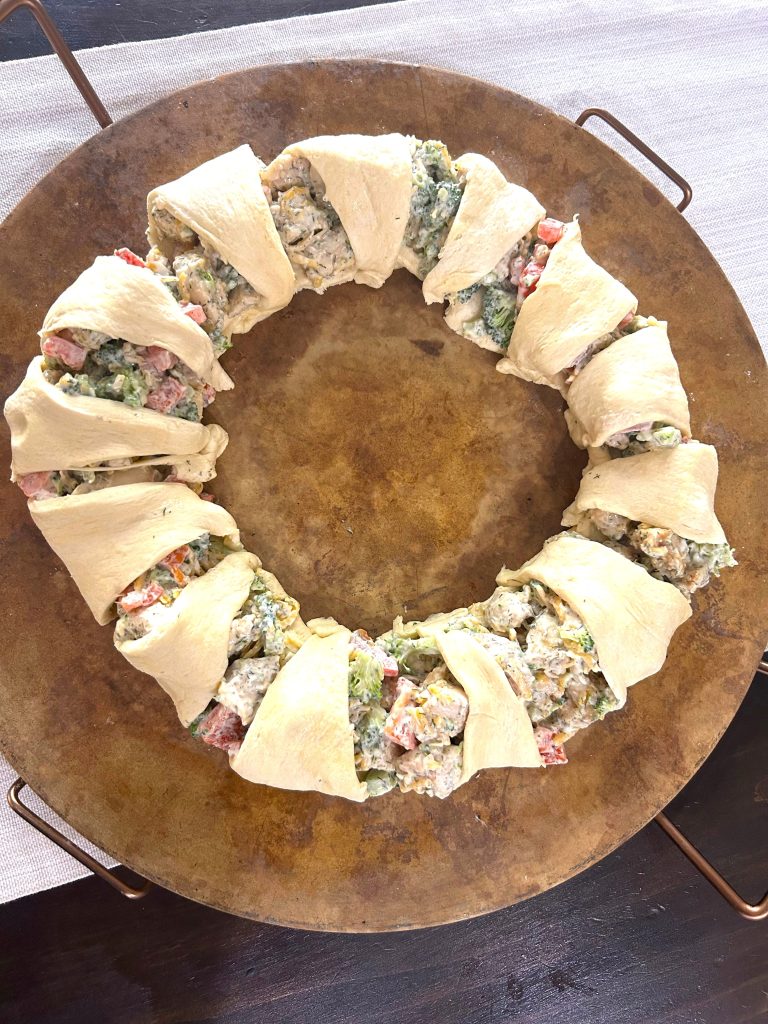 A baking stone with a completely assembled crescent roll ring filled with brcocoli braid mixture