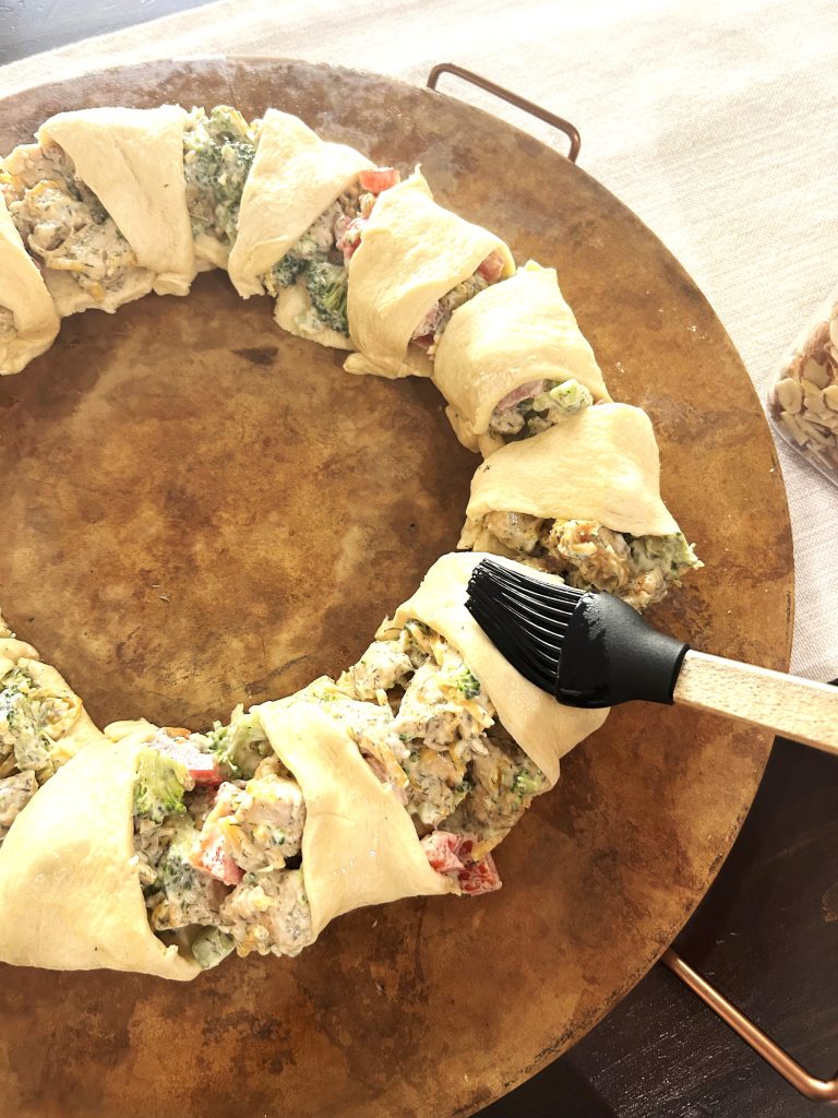 An assembled chicken broccoli braid being basted with a basting brush with egg whites