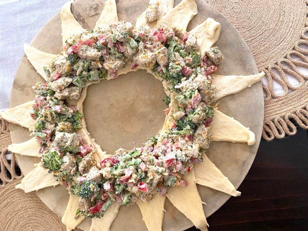 A baking stone on a pretty table with broccoli mix on inside of crescent roll ring, ready to be assembled into a braid