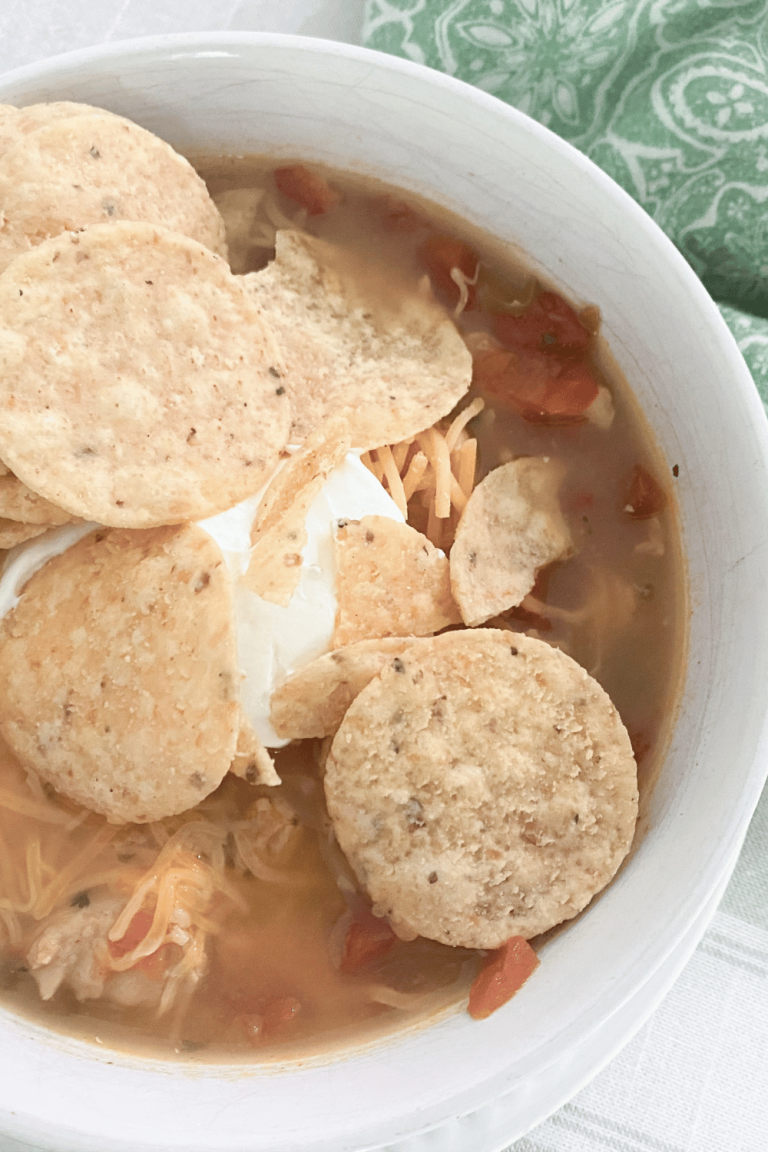 Chicken soup topped with sour cream and tortilla chips in a pretty bowl