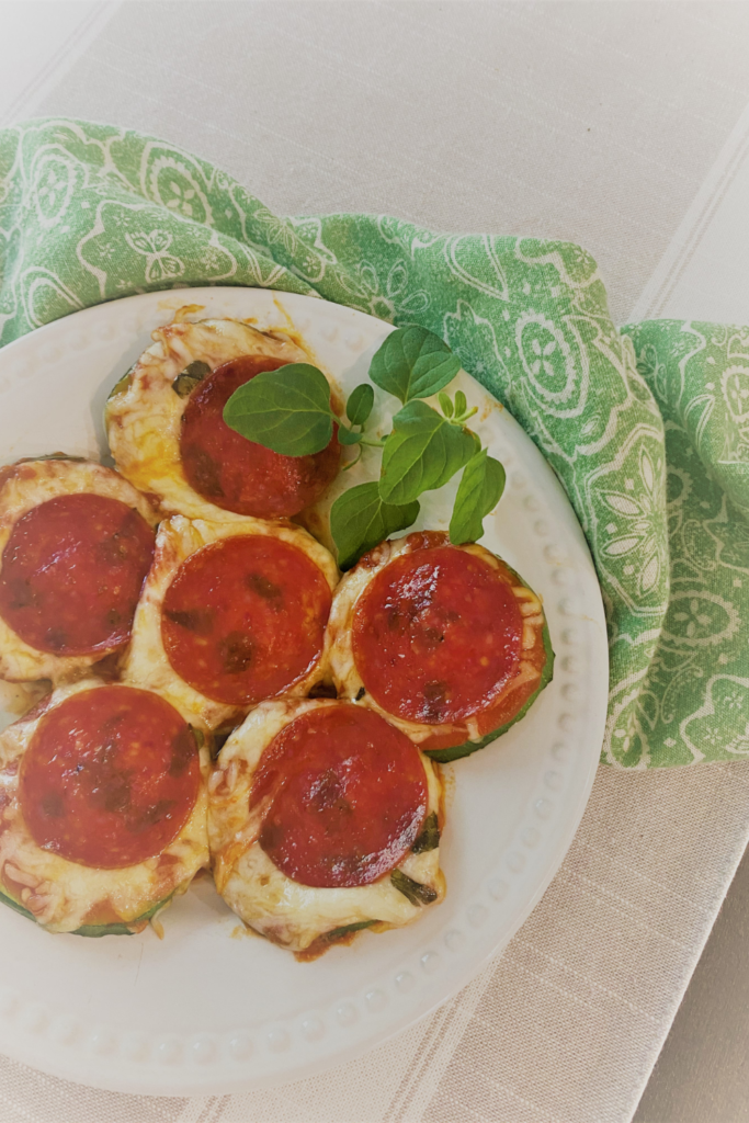 A plate of zucchini pizza bake on a white plate with a green paisley napkin and some fresh oregano