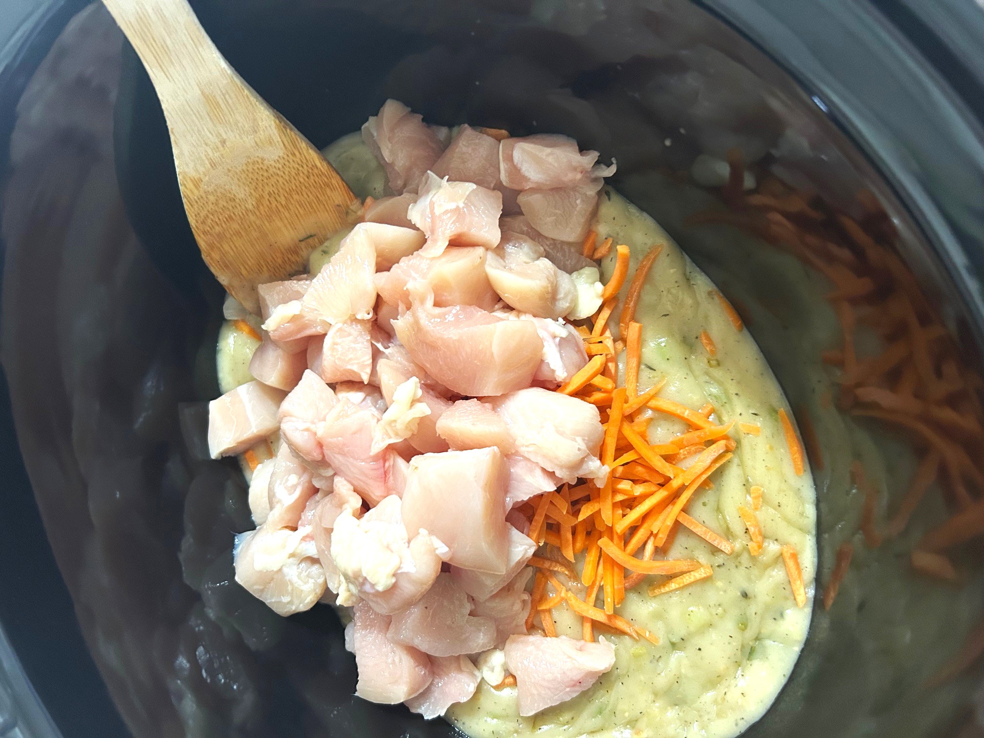 a black crockpot liner with chunks of raw chicken, matchsticks carrots, and chicken broth mixture ready to cook into soup