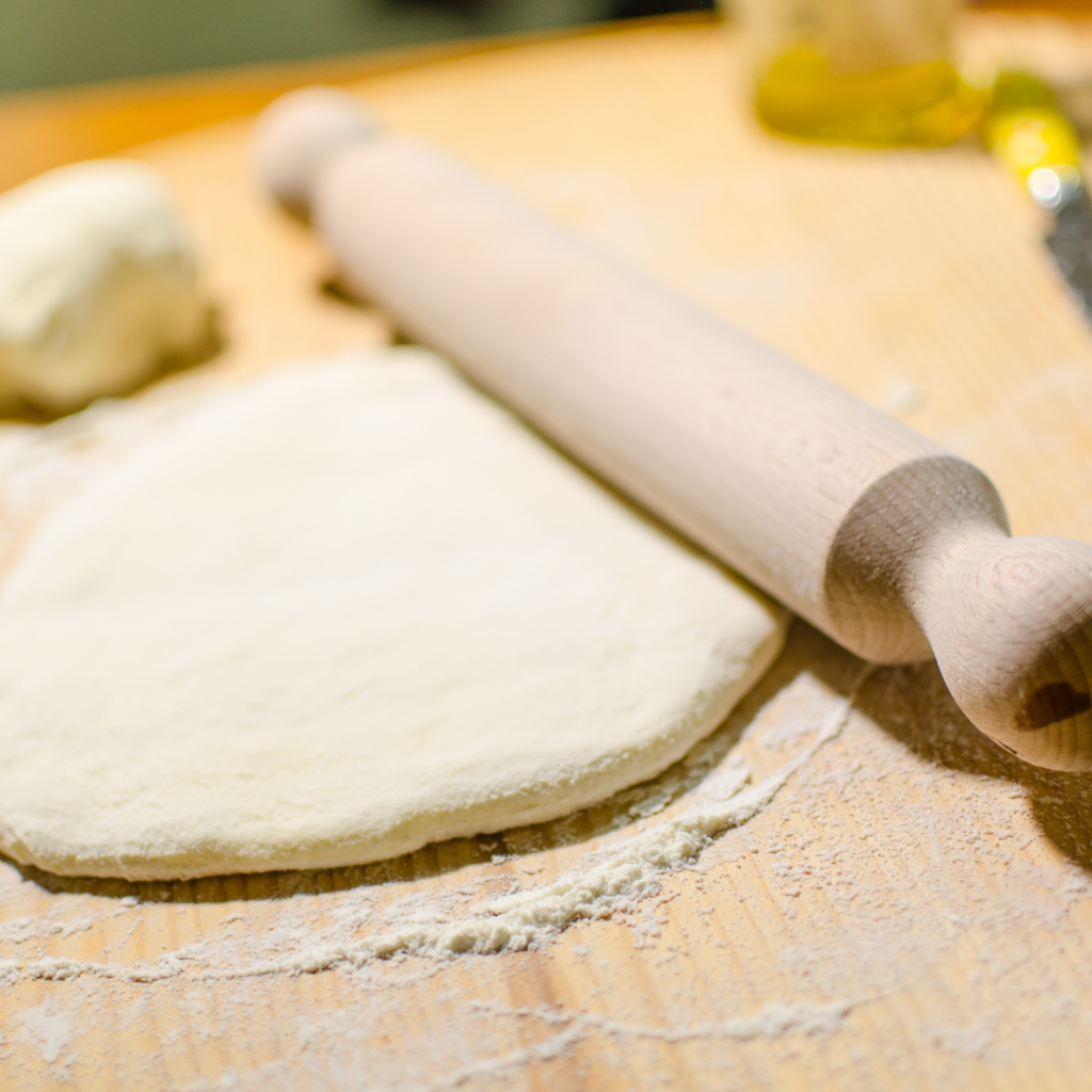 A close up picture of rolled out homemade pizza dough with a wooden rollling pin