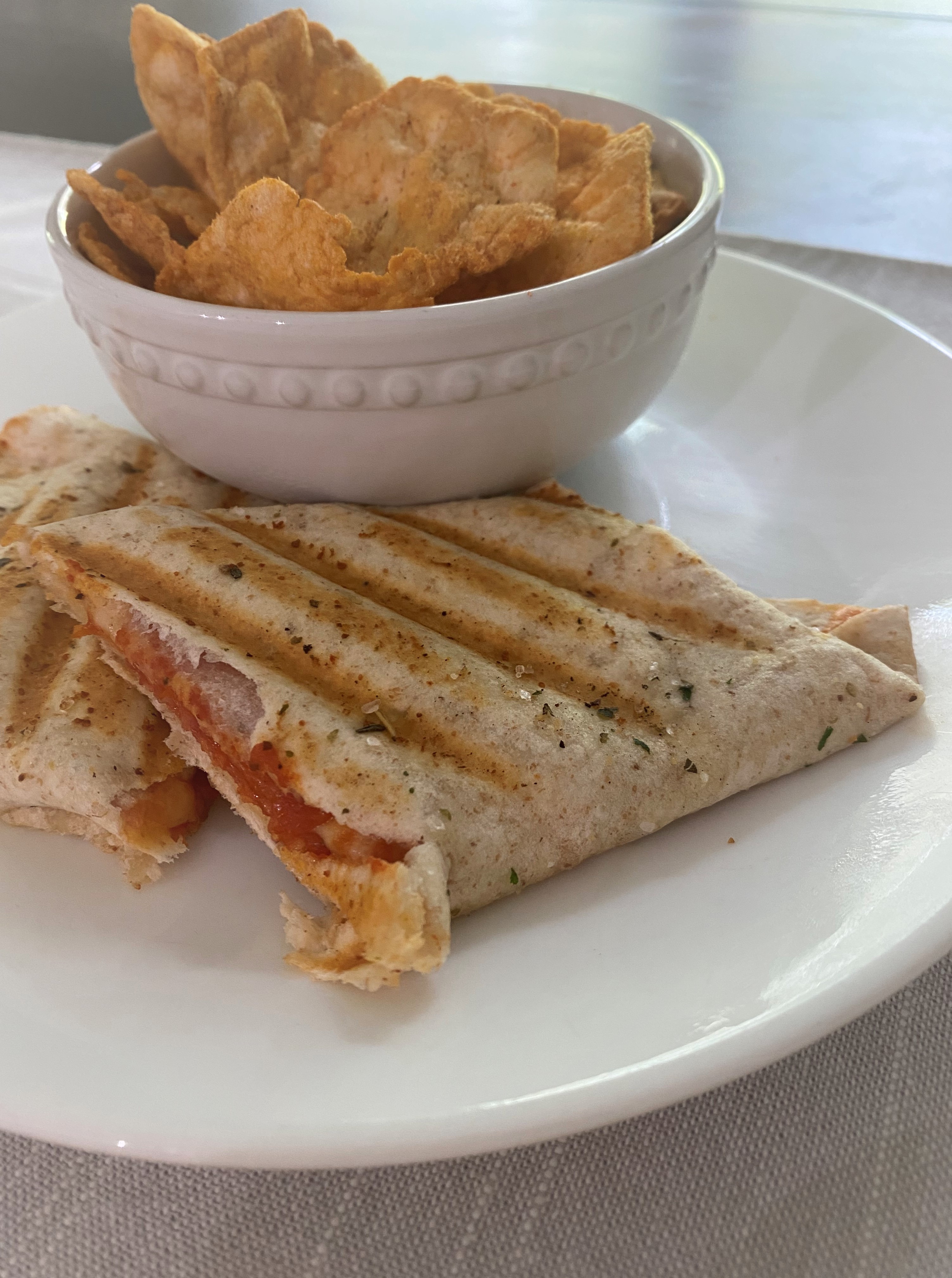 A pizza wrap fresh off the panini press, cut in half on a white plate with a side of chips