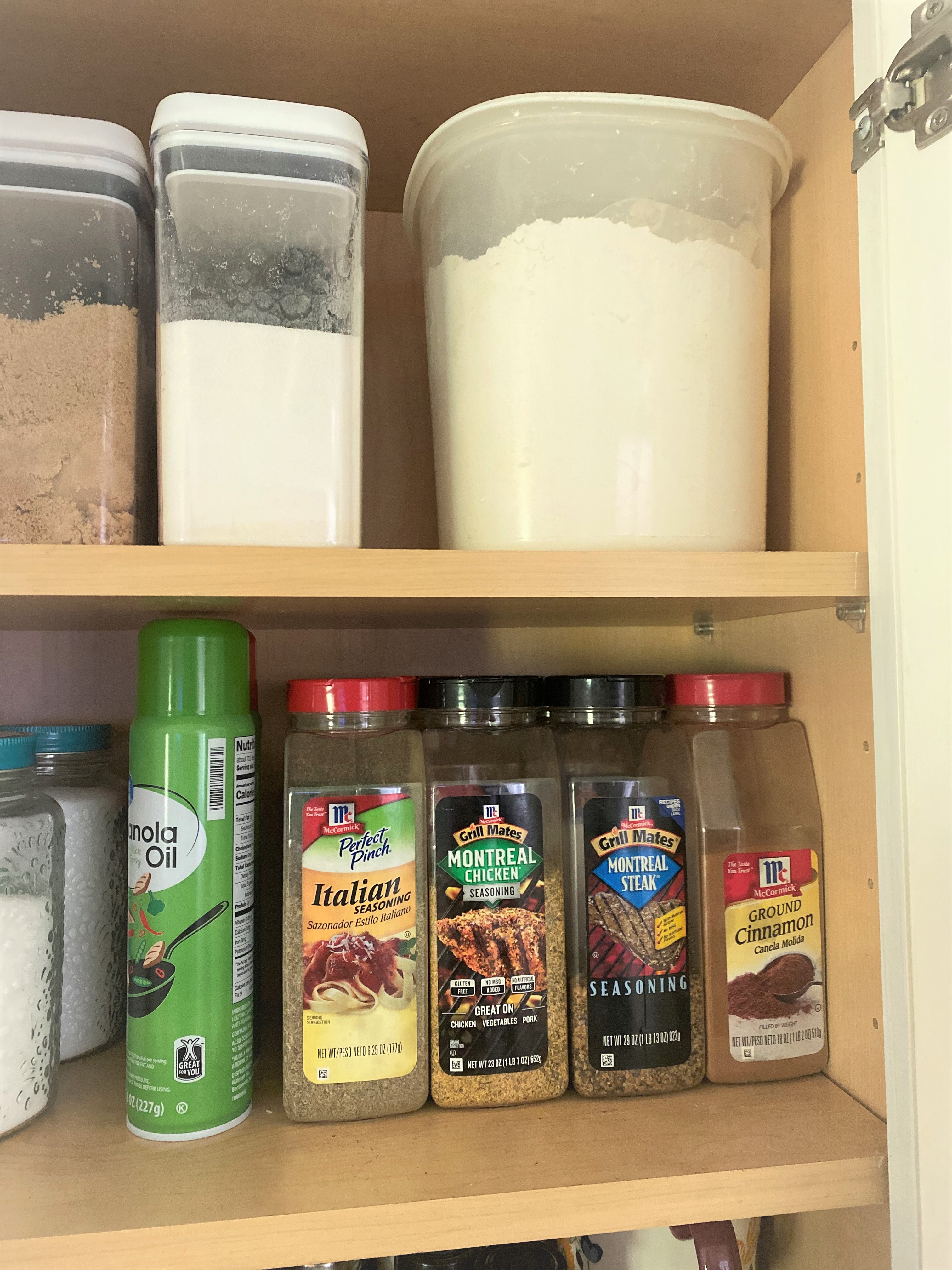 An open kitchen cabinet displaying some large sized spice containers and baking ingredients