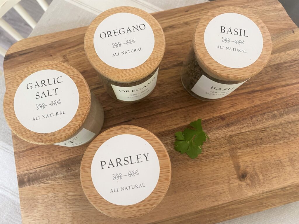 A few glass jars with bamboo lids with pretty simple white spice labels on a wooden cutting board with some oregano leaves for added effect