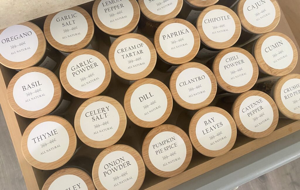 A finished drawer of glass spice jars with wooden lids with white labels, organized and ready to use