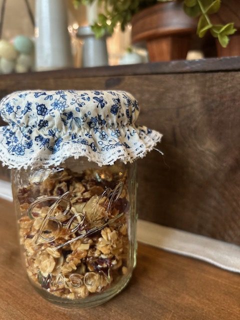A Ball mason jar of homemade granola covered in a blue floral and lace jar topper