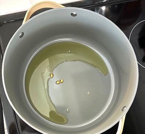 a white stock pot on a black stovetop with some oil and a few popcorn kernels waiting to pop