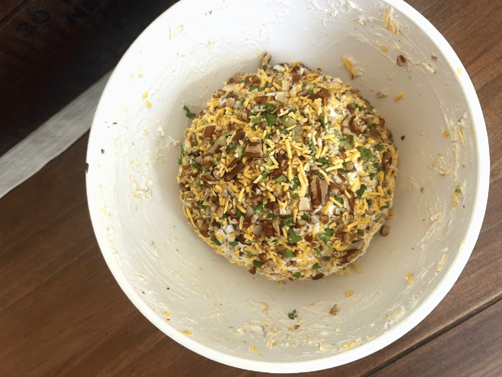 A white mixing bowl of a bacon cheddar cheese ball topped with a crumbly topping