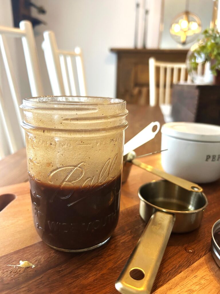 A close up of a mason jar half full of mixed homemade balsamic vinaigrette dressing